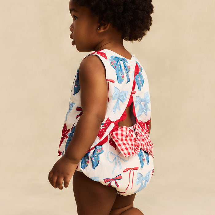 Child wearing a colorful outfit with bow patterns on a beige background