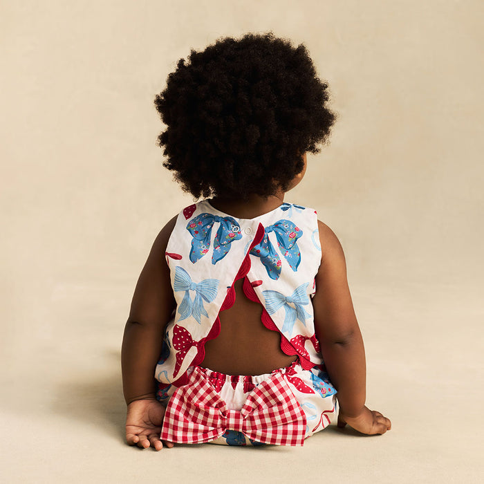 Child wearing a colorful outfit with bow pattern on a beige background