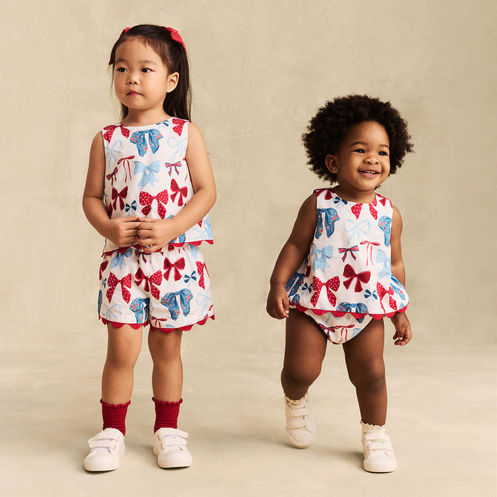 Two children wearing matching outfits with bow patterns on a beige background
