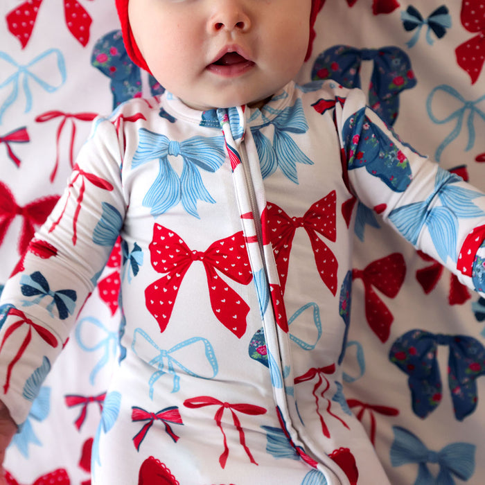 Baby wearing a onesie with red and blue bow pattern on a matching background