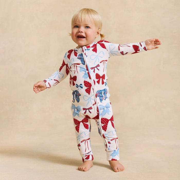 Child wearing a colorful onesie with bow patterns on a beige background