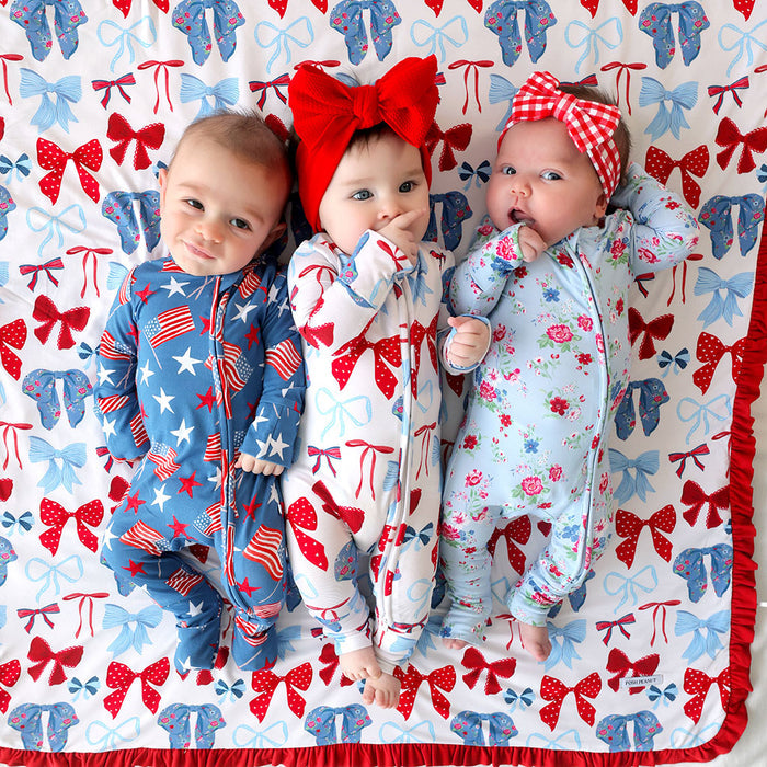 Three babies in colorful outfits lying on a patterned blanket with bows.