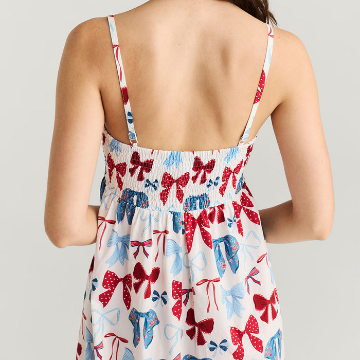 Back view of a person wearing a dress with red, blue, and white bow pattern on a plain background