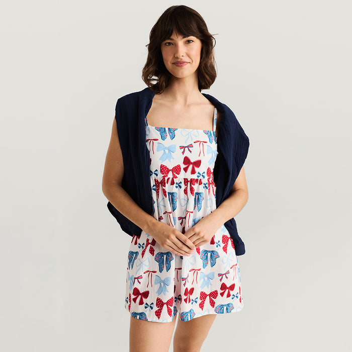 Woman wearing a dress with bow pattern and navy cardigan on a light gray background