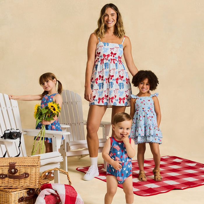 Woman and three children in matching outfits standing on a red and white checkered blanket with picnic items.