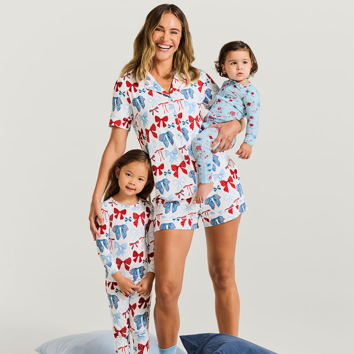 Woman and two children wearing matching pajama sets with a bow pattern on a plain background