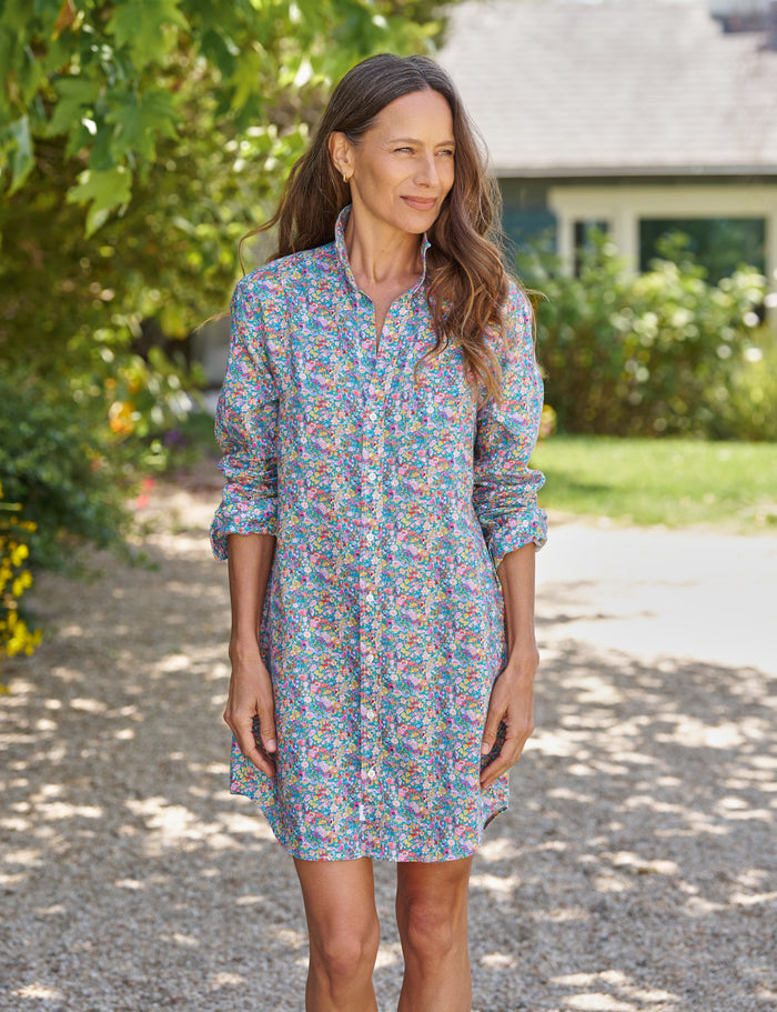 Woman wearing a floral dress standing on a gravel path with greenery and a house in the background