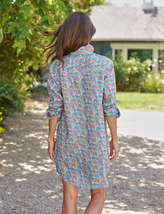 Woman in a colorful dress walking away from the camera on a gravel path with greenery and a house in the background.