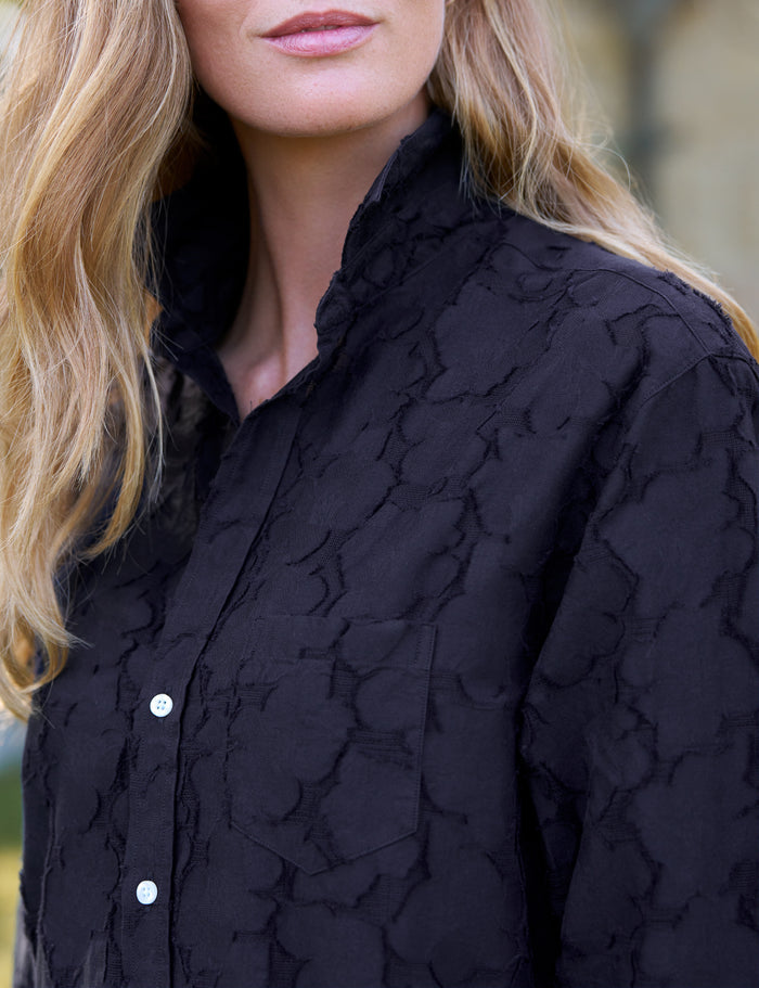 Close-up of a woman wearing a black textured dress with white buttons.