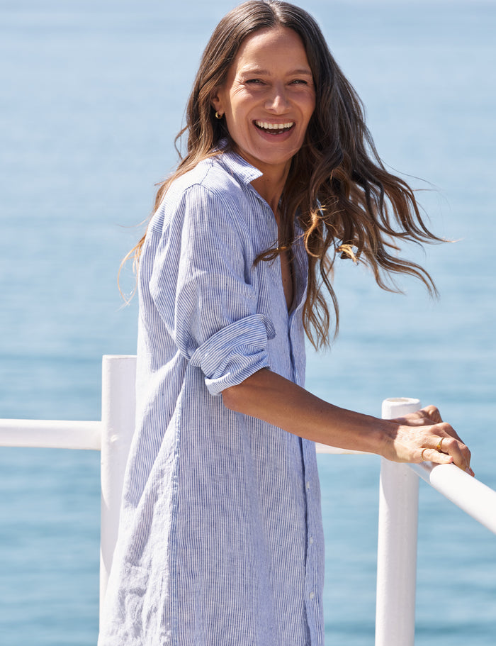 Woman in a blue and white striped dress standing by a body of water.