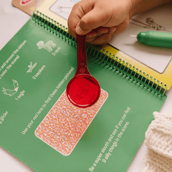little hand holds red magnifying lens above hidden picture panel to reveal additional puzzles