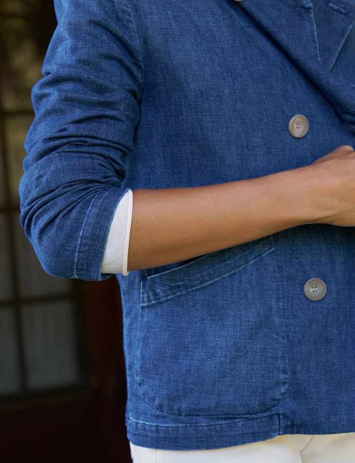 Close-up of a person wearing a blue denim-style blazer or jacket with rolled sleeves and visible white shirt cuffs underneath, against an indoor background.