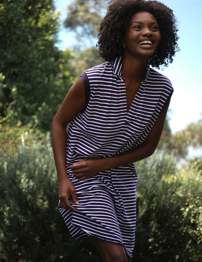 Woman wearing a navy and white striped dress standing outdoors with greenery in the background