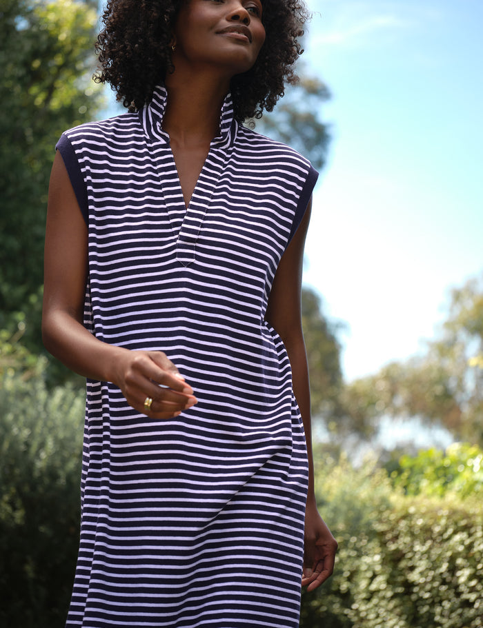 Woman wearing a navy and white striped dress outdoors with greenery in the background