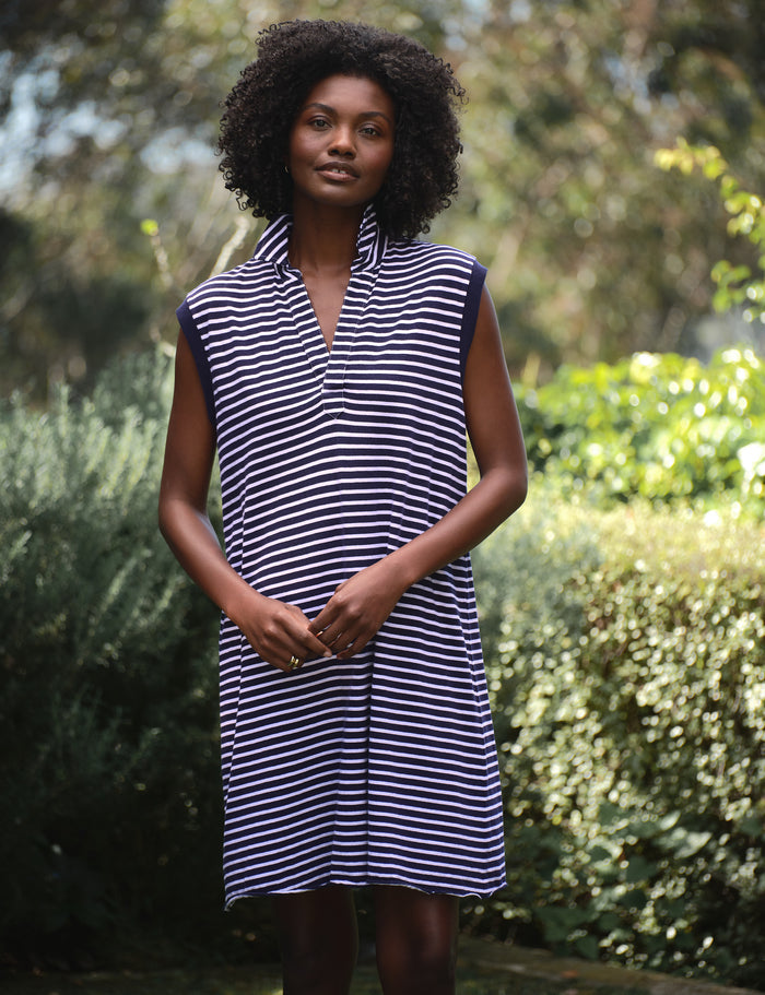 Woman wearing a navy and white striped dress standing outdoors with greenery in the background
