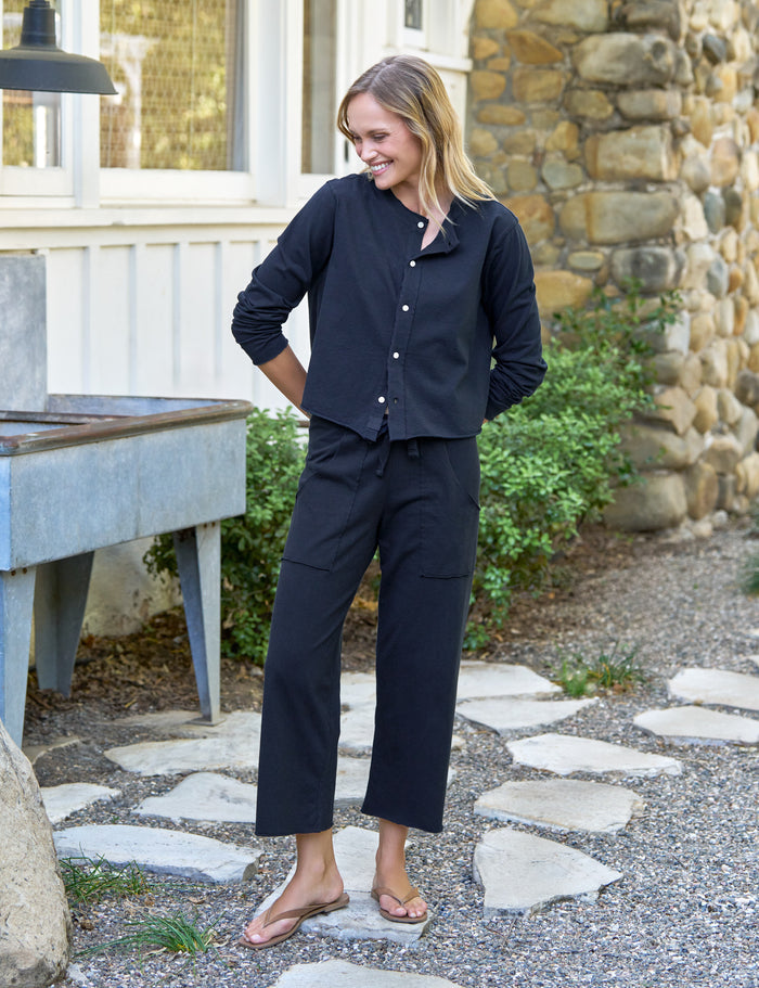 Woman in navy outfit standing outdoors near a stone wall and garden.
