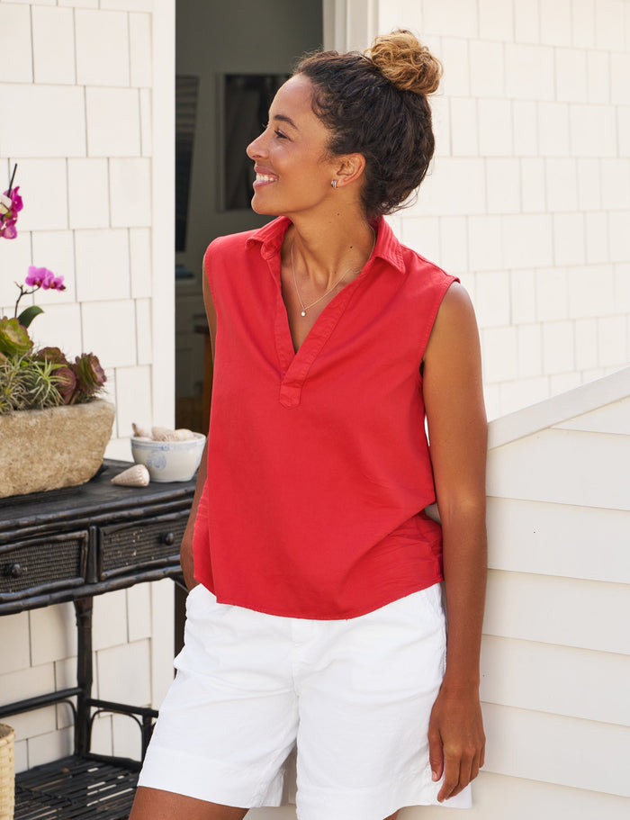 Woman in a red shirt and white shorts standing on a porch.