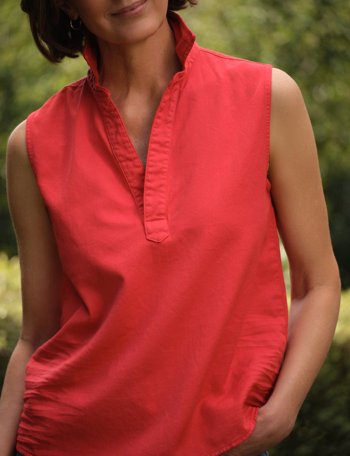Woman wearing a red sleeveless top with a blurred green background