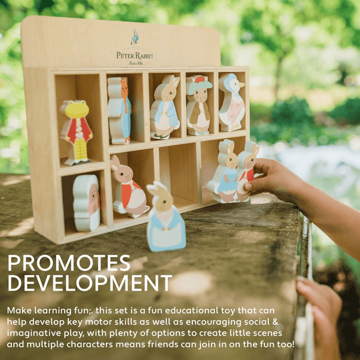 little girls hands holds peter rabit characters in beside display shelf on a wooden outdoor table with trees in background