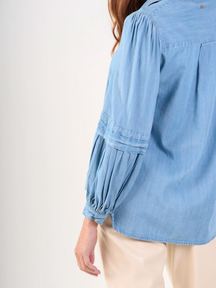 A person wearing the Oxford light blue balloon sleeve blouse and cream-colored pants, shown from the back and side against a plain light background.