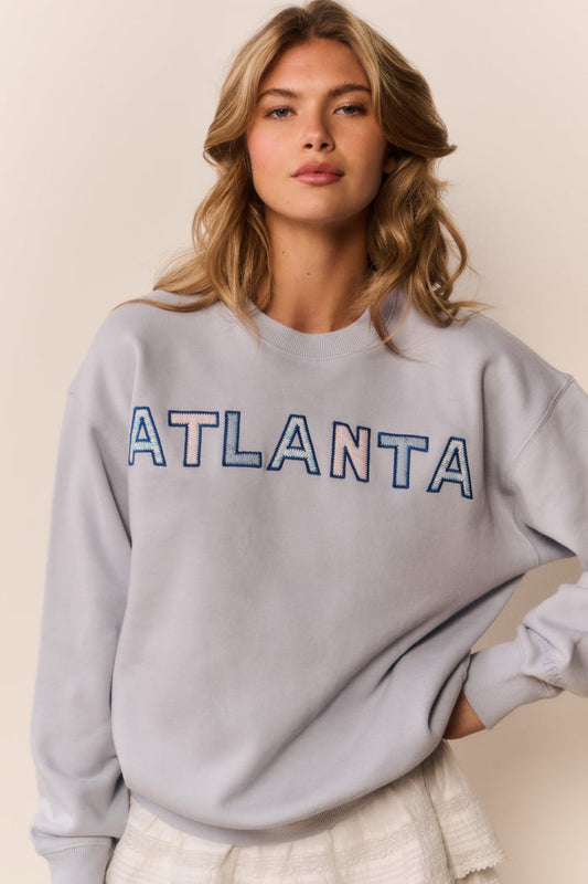 Woman wearing white mini skirt with ruffles and grey pullover that says Atlanta across the front