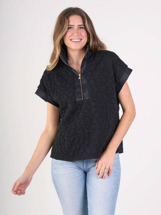 A woman with long brown hair smiles and poses against a plain white background, wearing the sporty sophistication of a Poppy Pullover and light blue jeans.
