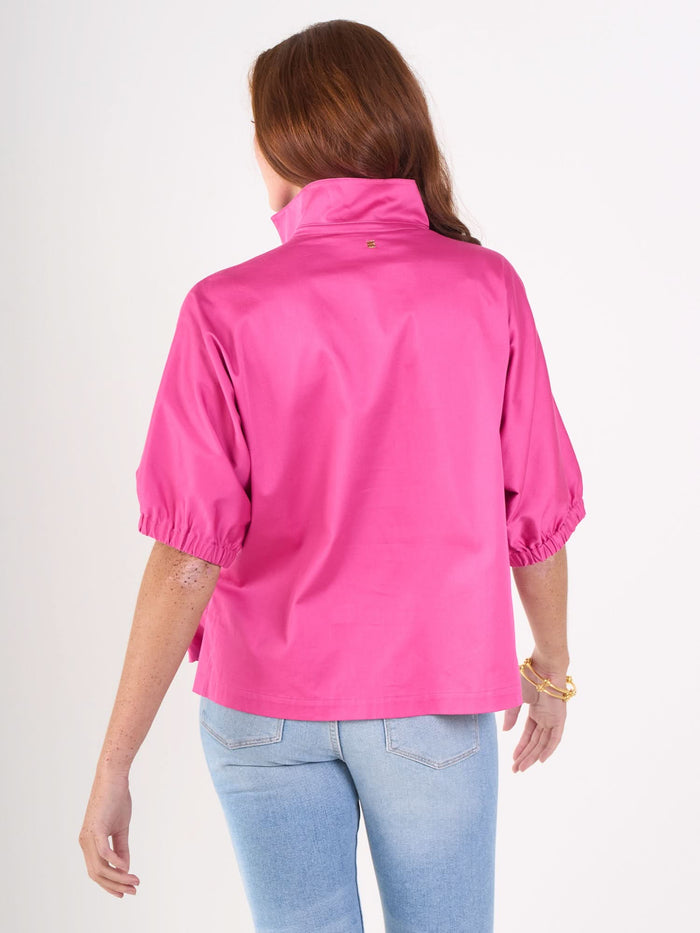 A woman with long brown hair wears the Poppy Top in bright pink cotton poplin and light blue jeans, standing with her back to the camera against a plain white background.