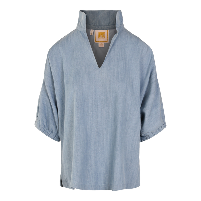 The Poppy Top is a light blue, loose-fitting top by Emily McCarthy with a V-neck, stand-up collar, and softly gathered sleeves in Denim Chambray for a relaxed style.