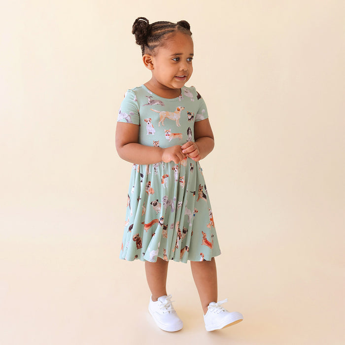 Girl wearing a green dog printed dress standing on a being background.
