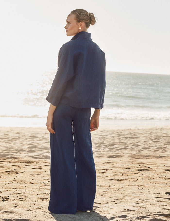 Woman in a navy outfit standing on a beach with ocean in the background