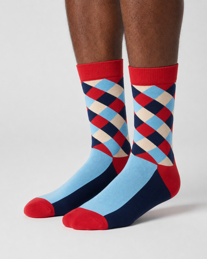 A pair of crew socks with a colorful argyle pattern on the upper leg and solid light blue, navy, and red sections on the lower half, shown worn on a person's legs against a light gray studio background.