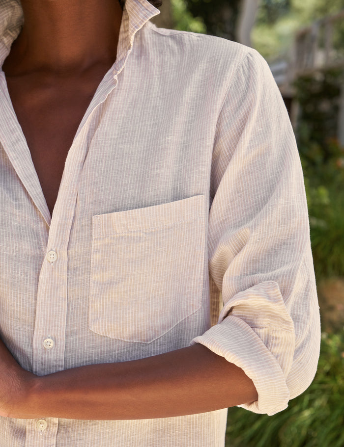 Person wearing a light-colored striped dress with rolled-up sleeves in an outdoor setting.