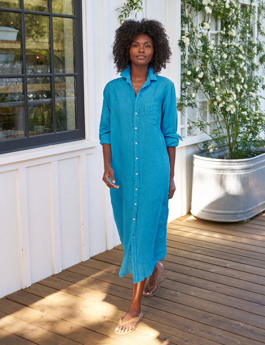 Woman wearing a blue dress standing on a wooden deck with plants in the background