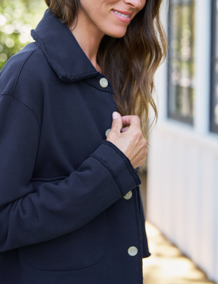 A woman wearing a dark navy blue coat with a collar and light-colored buttons, shown in a close-up outdoor shot.