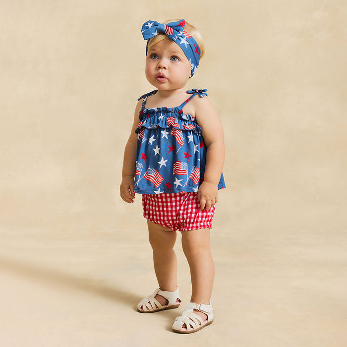 Baby girl wearing a red, white, and blue outfit with a matching headband on a beige background