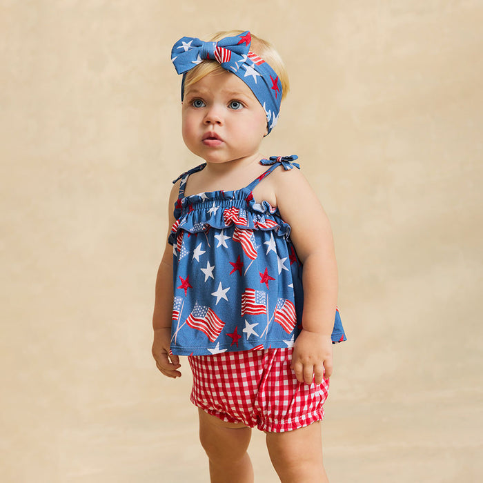 Baby wearing a red, white, and blue outfit with a matching headband on a beige background