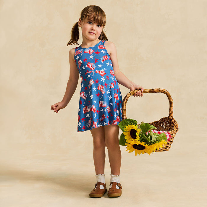 Young girl in a blue dress with American flag pattern holding a basket of sunflowers against a beige background