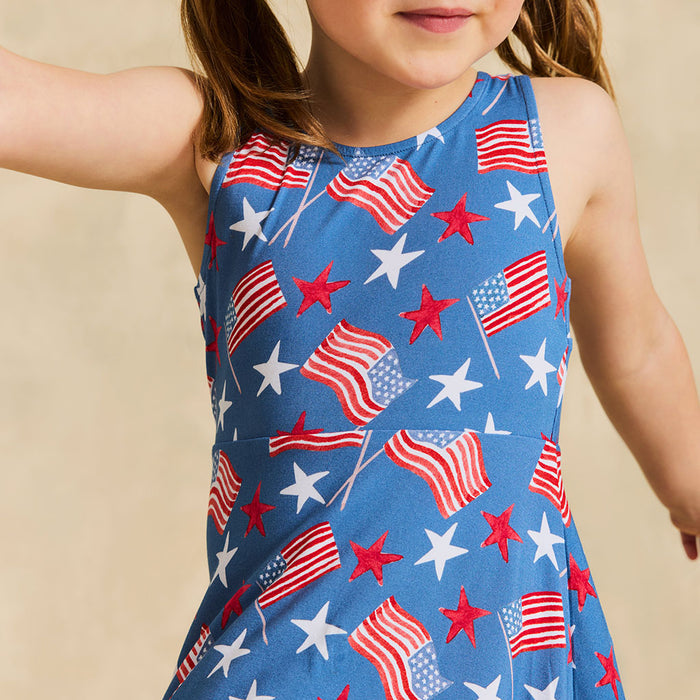 Child wearing a sleeveless dress with American flag pattern on a beige background