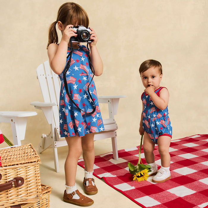 Two children in matching outfits with American flag pattern on a red checkered blanket.