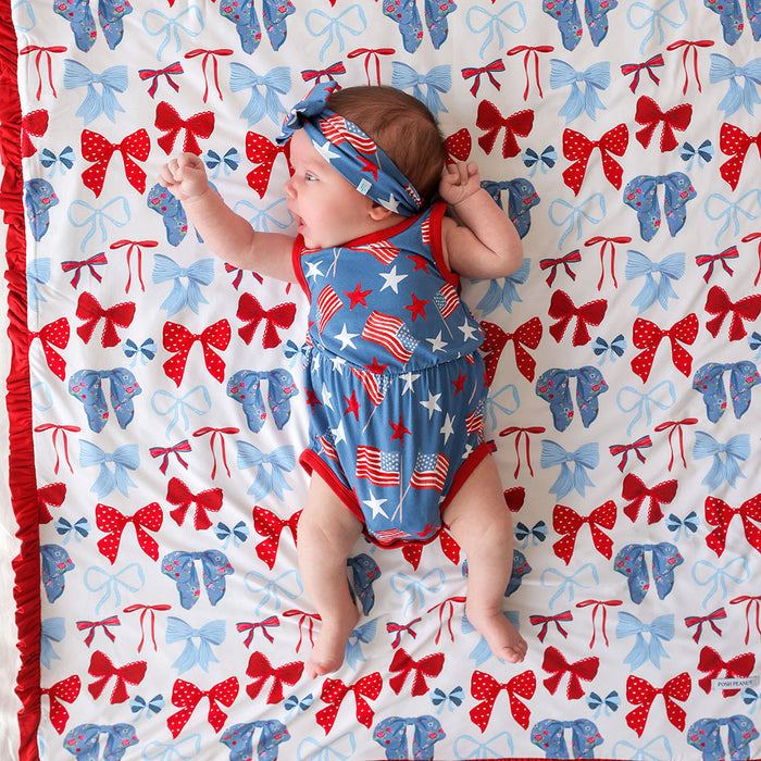Baby lying on a colorful patterned blanket with red, white, and blue colors.