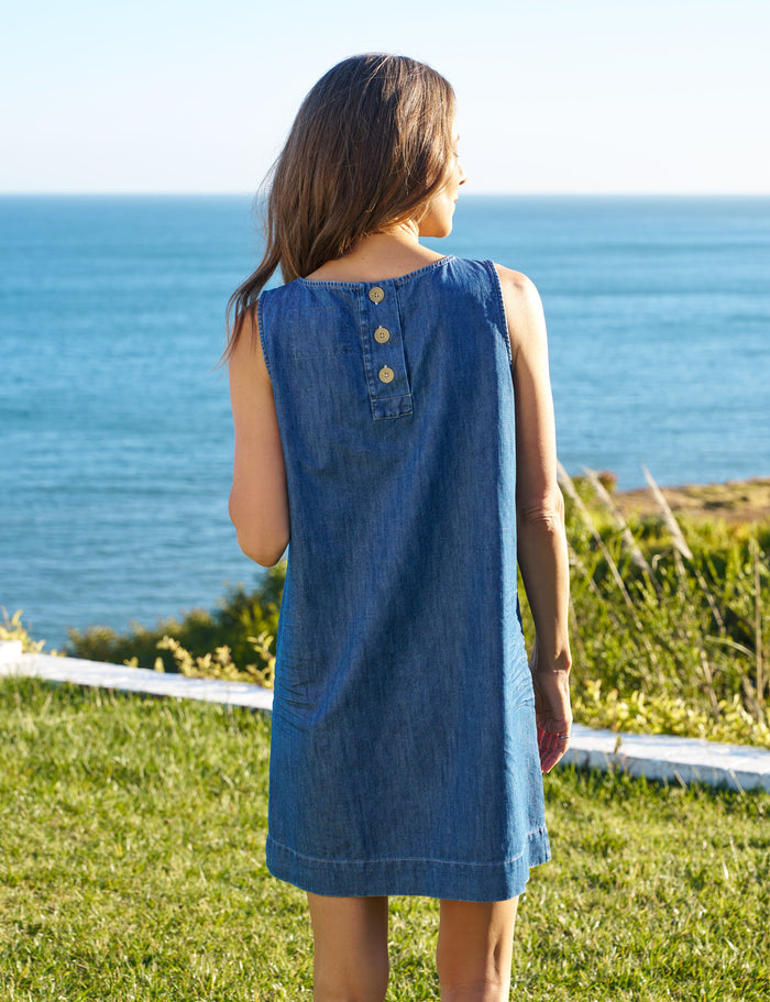 Woman in a blue dress standing on grass overlooking the ocean.