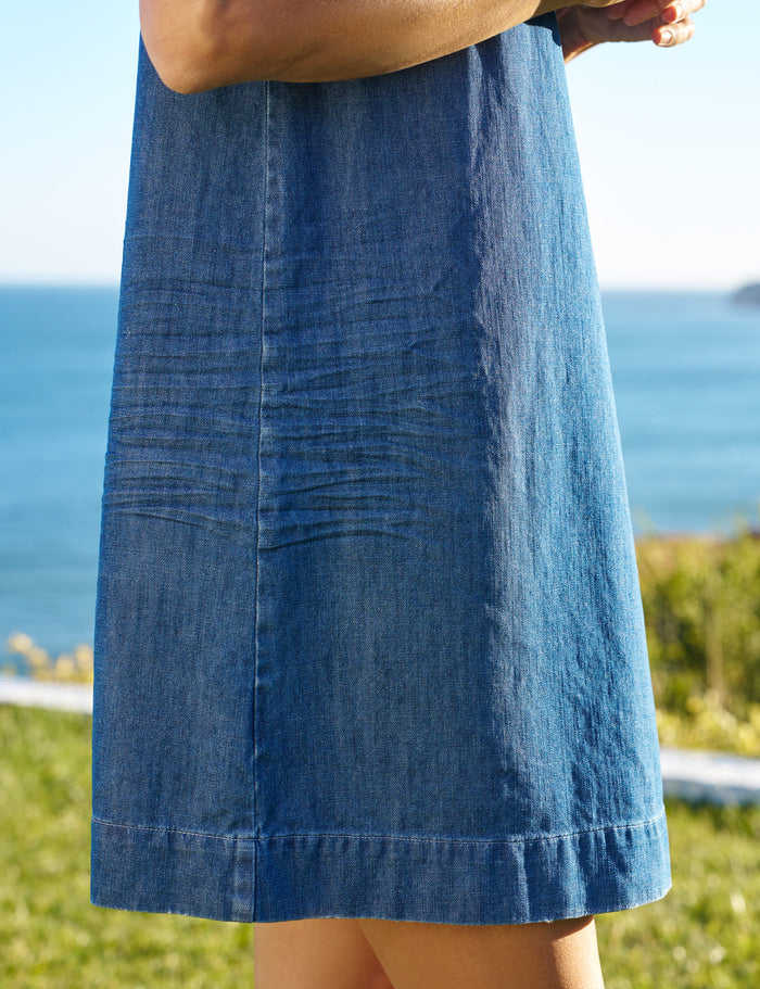 Person wearing a blue denim dress with a blurred background of water and sky