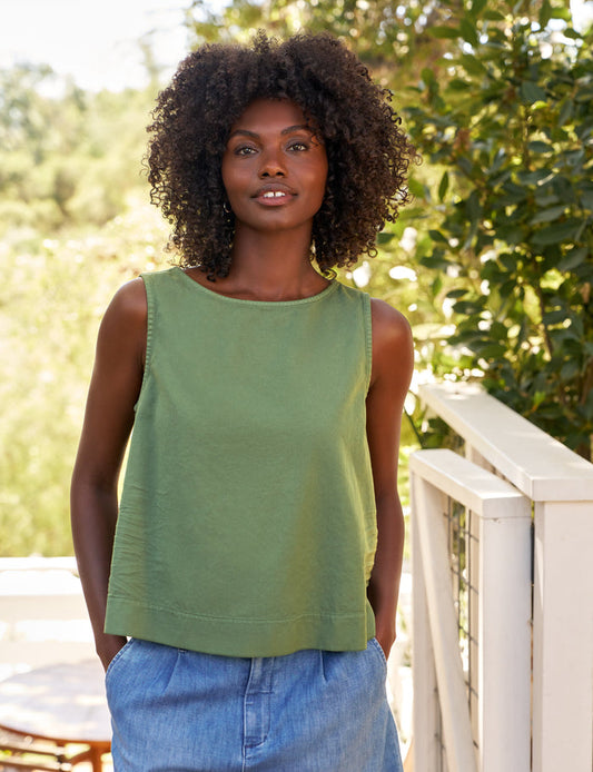 Woman wearing a green sleeveless top and blue jeans standing outdoors with trees in the background