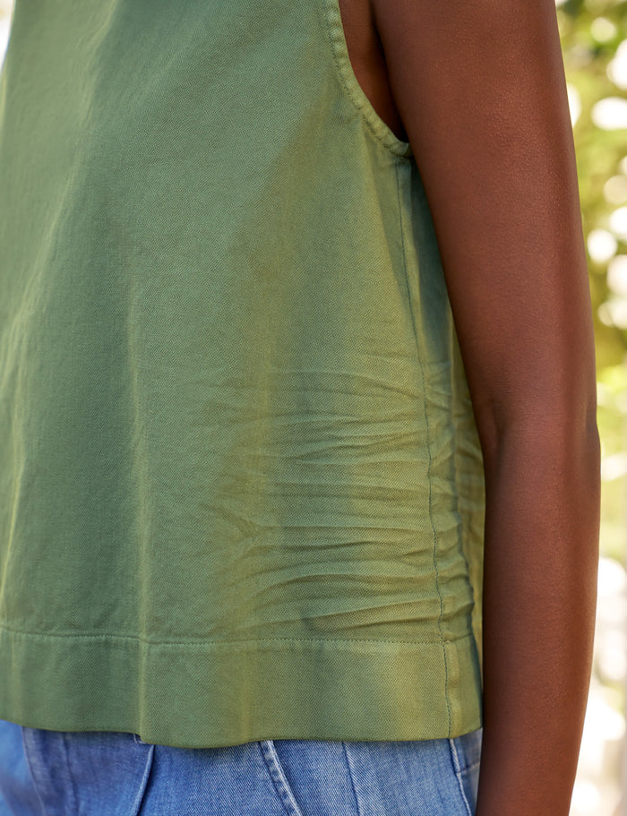 Green sleeveless top worn by a person with a blurred natural background