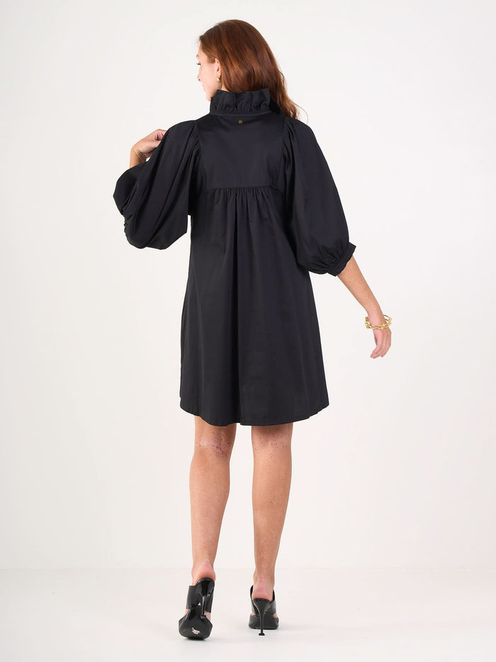 A woman with long hair faces away from the camera against a plain white background, wearing the Stella Dress with puffy sleeves and black heels.