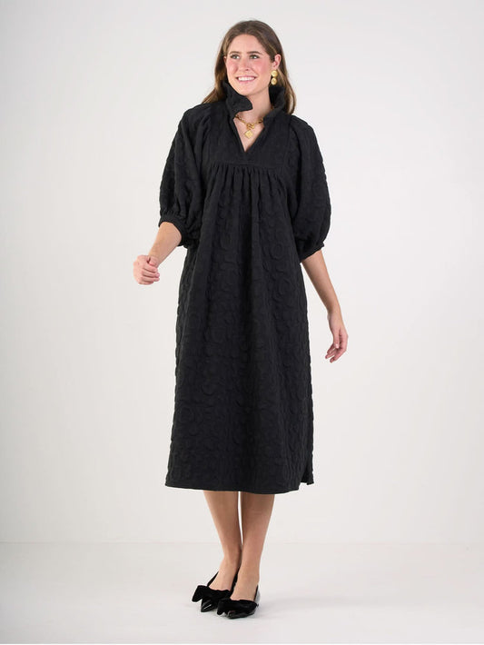 A woman smiles against a plain background, wearing the loose-fitting Stella Midi dress with embossed cheetah texture and elbow-length puff sleeves, paired with black bow flats plus gold earrings and necklace.